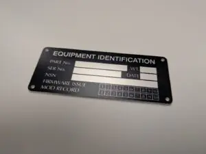 A rectangular black metal plate with white-etched text and four corner mounting holes. Main Heading: "EQUIPMENT IDENTIFICATION" Technical Fields: Rows for "PART No.", "SER No.", "NSN", "WT.", "DATE", and "FIRMWARE ISSUE". Mod Record: Two rows of numbered boxes (1 through 10) for tracking equipment modifications.