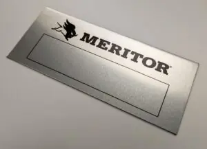 A rectangular, brushed aluminum brand plate featuring the Meritor logo in bold black capital letters. To the left of the text is a stylized graphic of a winged bull or beast. A large, rectangular black-bordered box is positioned below the branding for custom stamping or engraving.