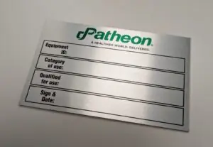 A rectangular, brushed aluminum identification plate with the "Patheon" logo in green and the slogan "A HEALTHIER WORLD. DELIVERED." etched below it. The plate features four horizontal boxes for manual data entry: Equipment ID: Top field for specific machine identification. Catagory of use: Second field for application type (note: "Catagory" is spelled as shown on the plate). Qualified for use: Third field for compliance or safety status. Sign & Date: Bottom field for technician verification.
