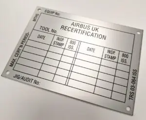 A large, rectangular brushed metal certification plate designed for aviation maintenance tracking. The plate includes mounting holes in all four corners and a clean, black-etched grid for manual data entry. The layout includes: Main Heading: "AIRBUS UK RECERTIFICATION" Top/Bottom Fields: Labels for "EQUIP No:", "TOOL No:", and "JIG/AUDIT No:" Side Markings: Vertical text for "MAX. CERT'N PERIOD - MTHS" on the left and "TRS 03-064 ISS" on the right Log Grid: Columns for "DATE", "INSP. STAMP", and "800 ISS." repeated across two sections to record multiple inspection intervals